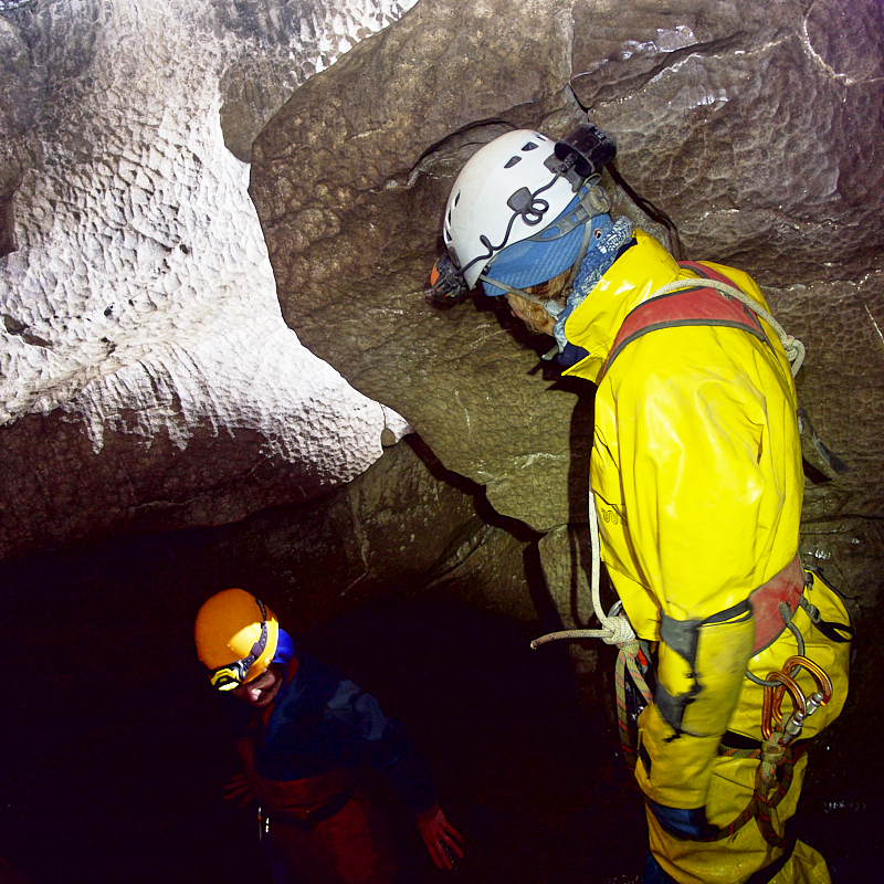 yellow caving suit looks down at caver descending into black