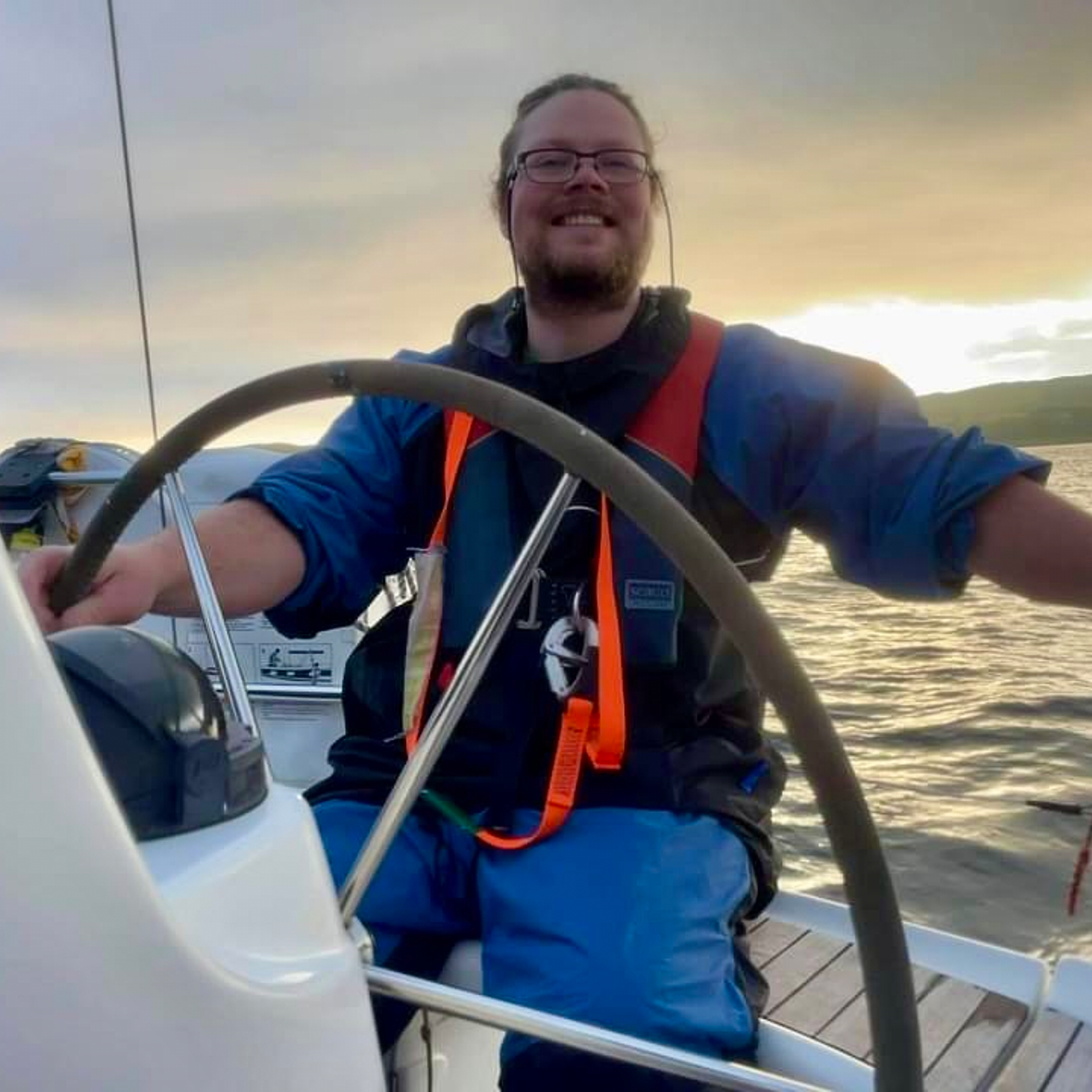Happy gent with sunset behind as he steers boat 