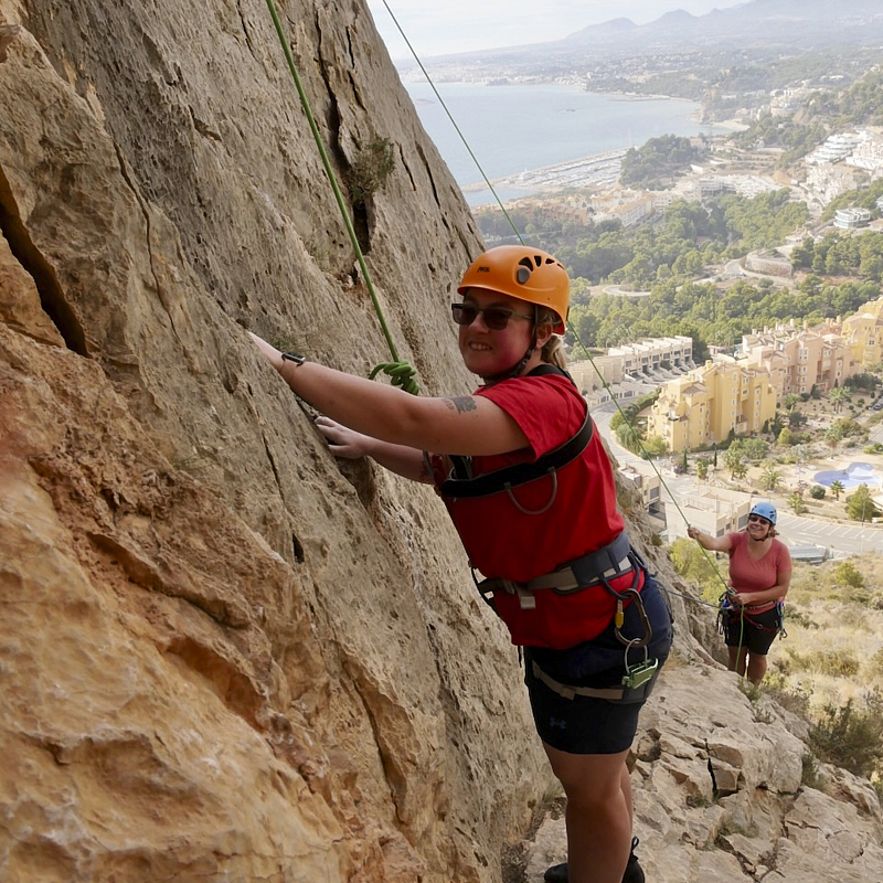 Lady climbs on spanish rock with sea far below