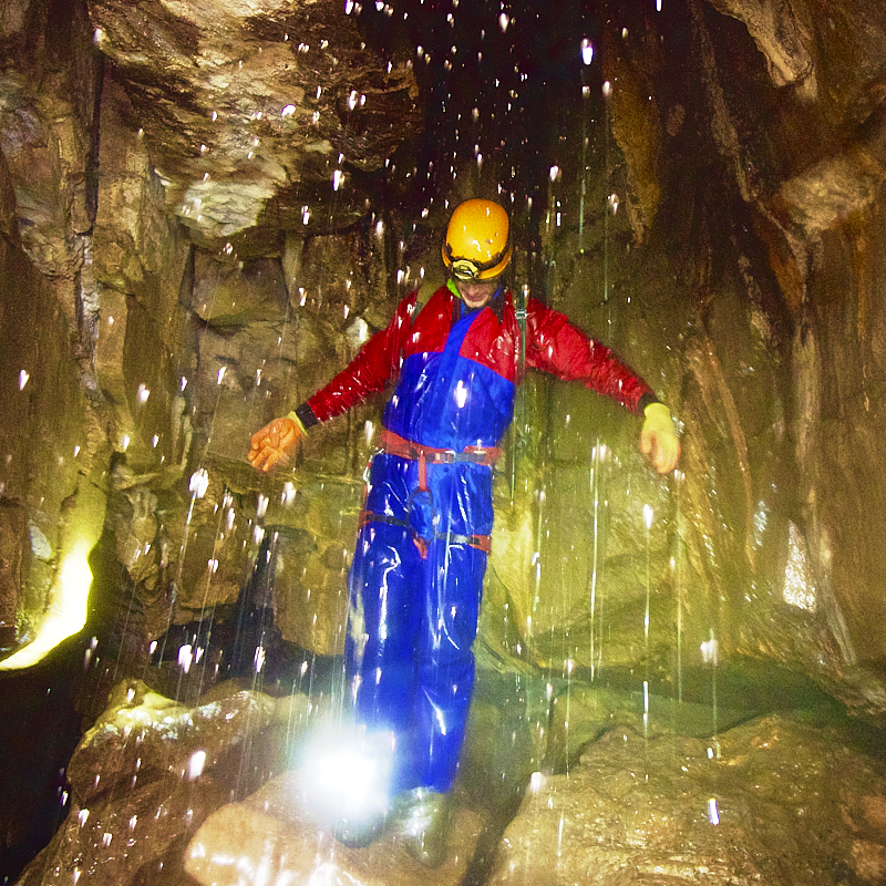 Person in blue and red caving suit stands amongst glowing droplets