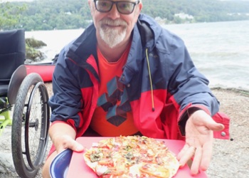 Man holds up fire cooked pizza.