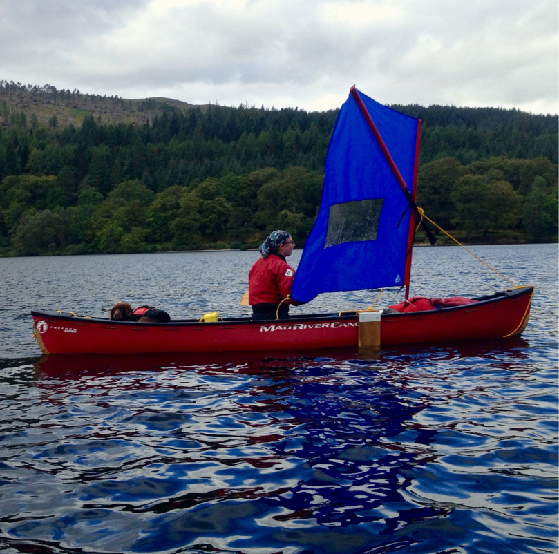 Canoe with a sail crosses loch.
