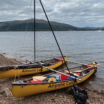 A sailing rigged canoe rests on the shore