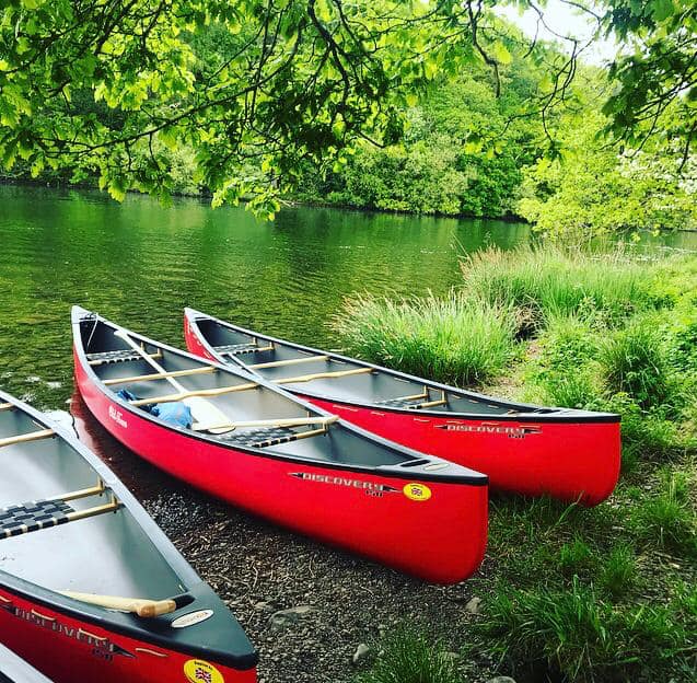 Canoe with a sail crosses loch.