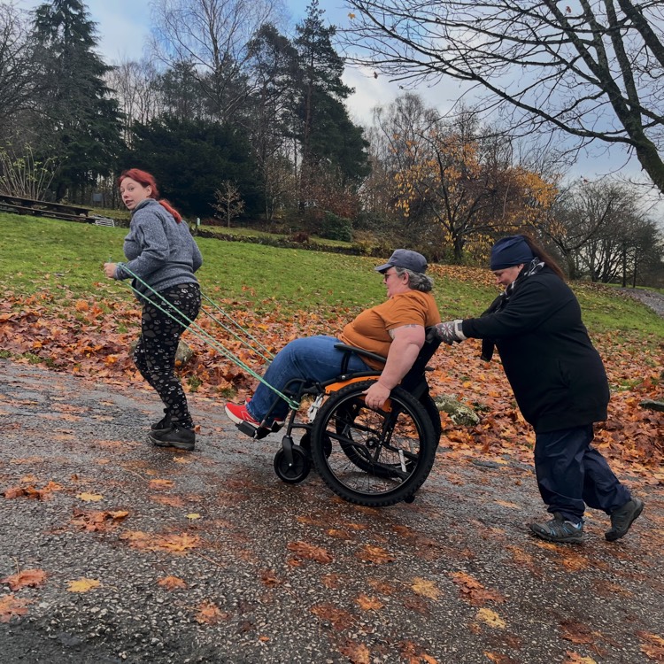 Wheelchair pushed and towed uphill by assistants 