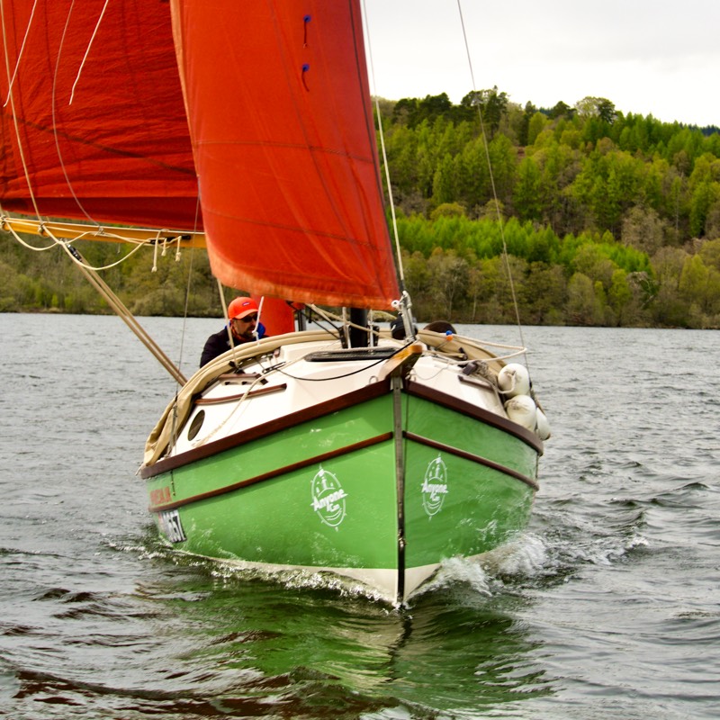 Green yacht surges under red sails